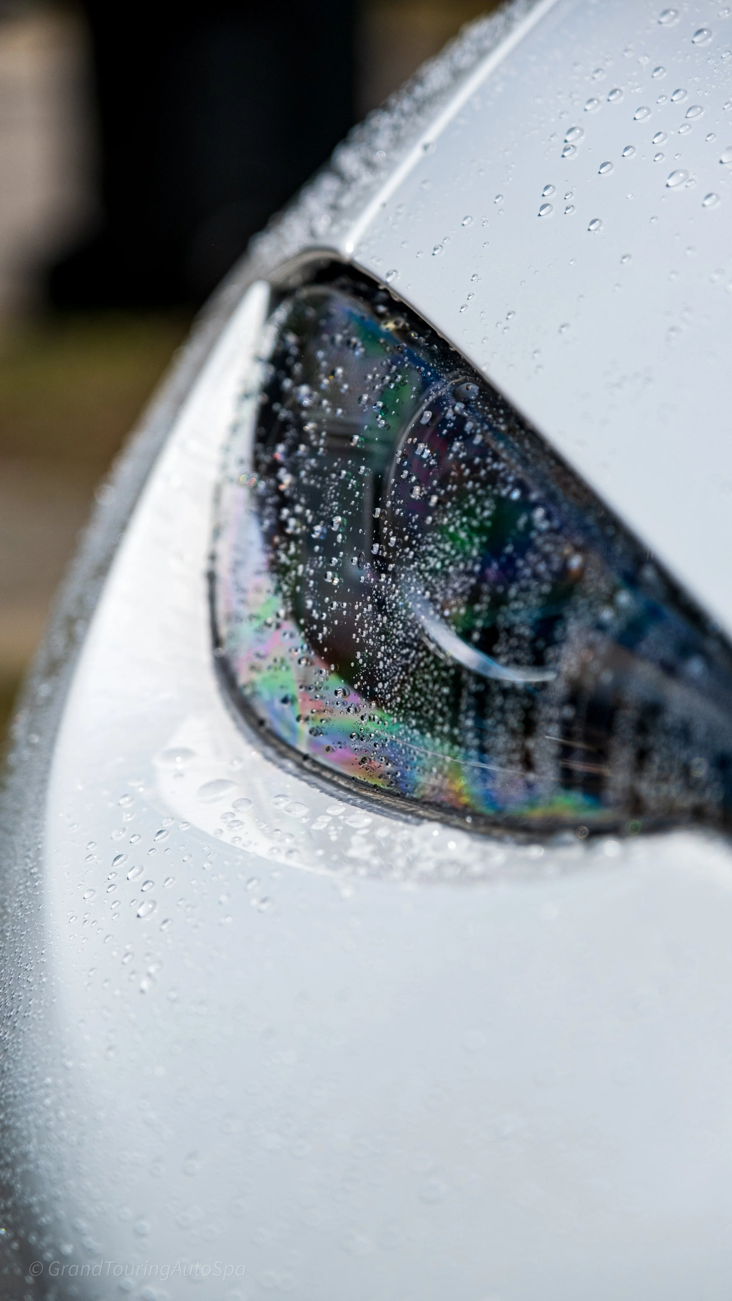 Close-up of a car headlight with raindrops on its surface.