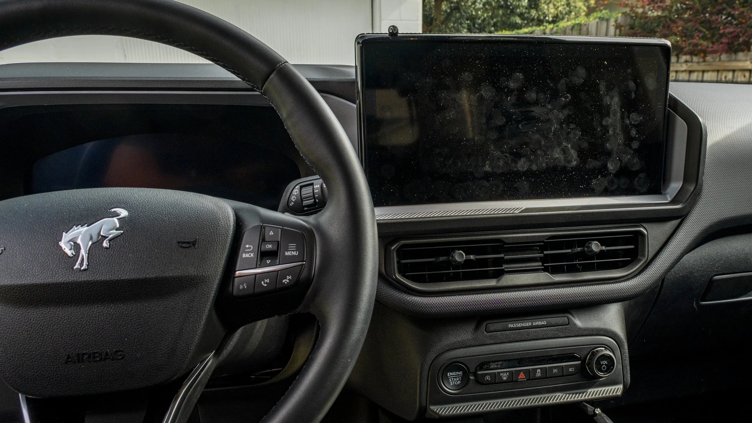 The image shows the interior dashboard of a vehicle, focusing on the steering wheel with a logo of a lion, and a large touchscreen display on the center console, surrounded by air vents and control buttons.