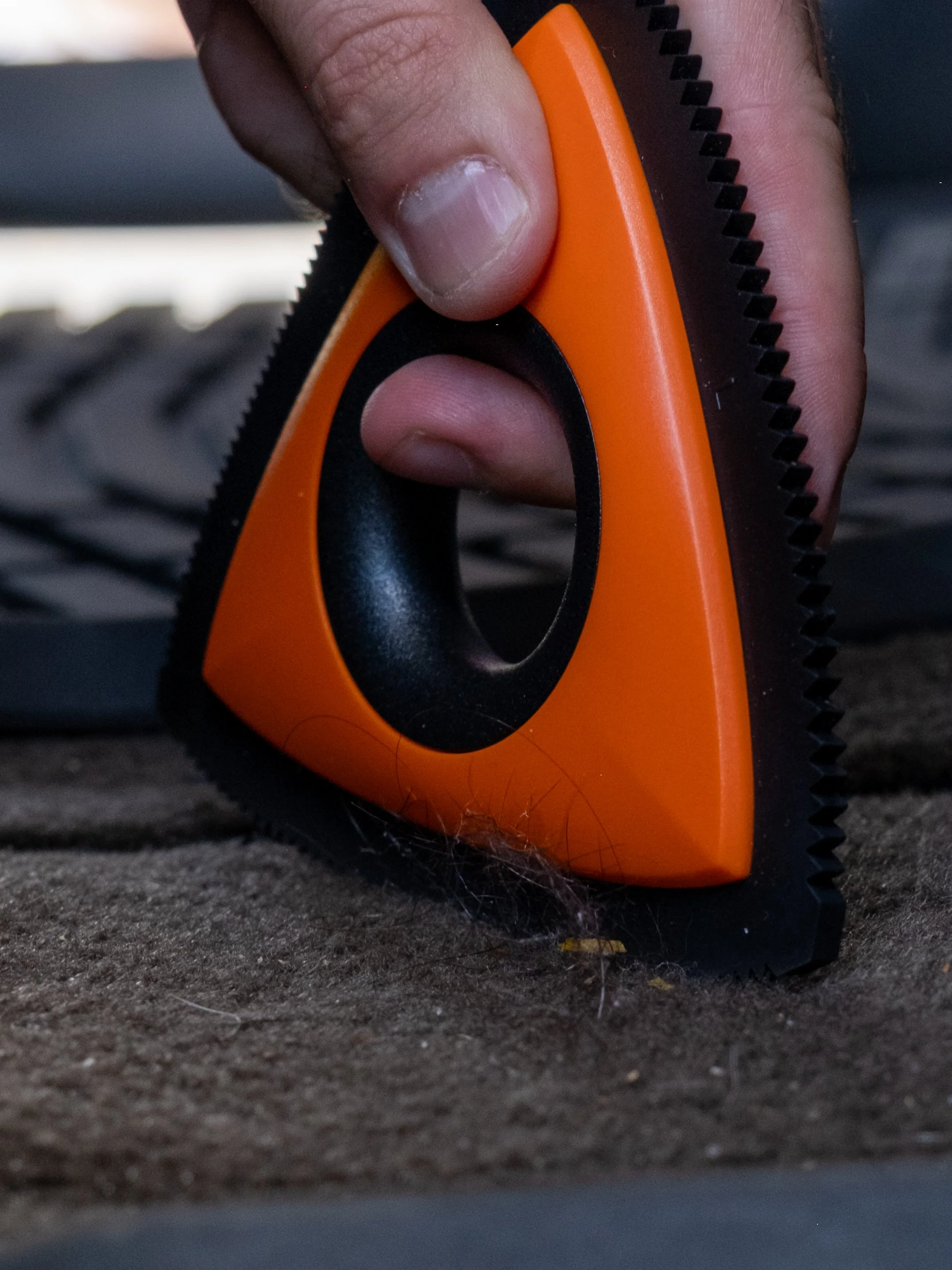 A hand holding an orange and black rotary cutter on a dark surface.