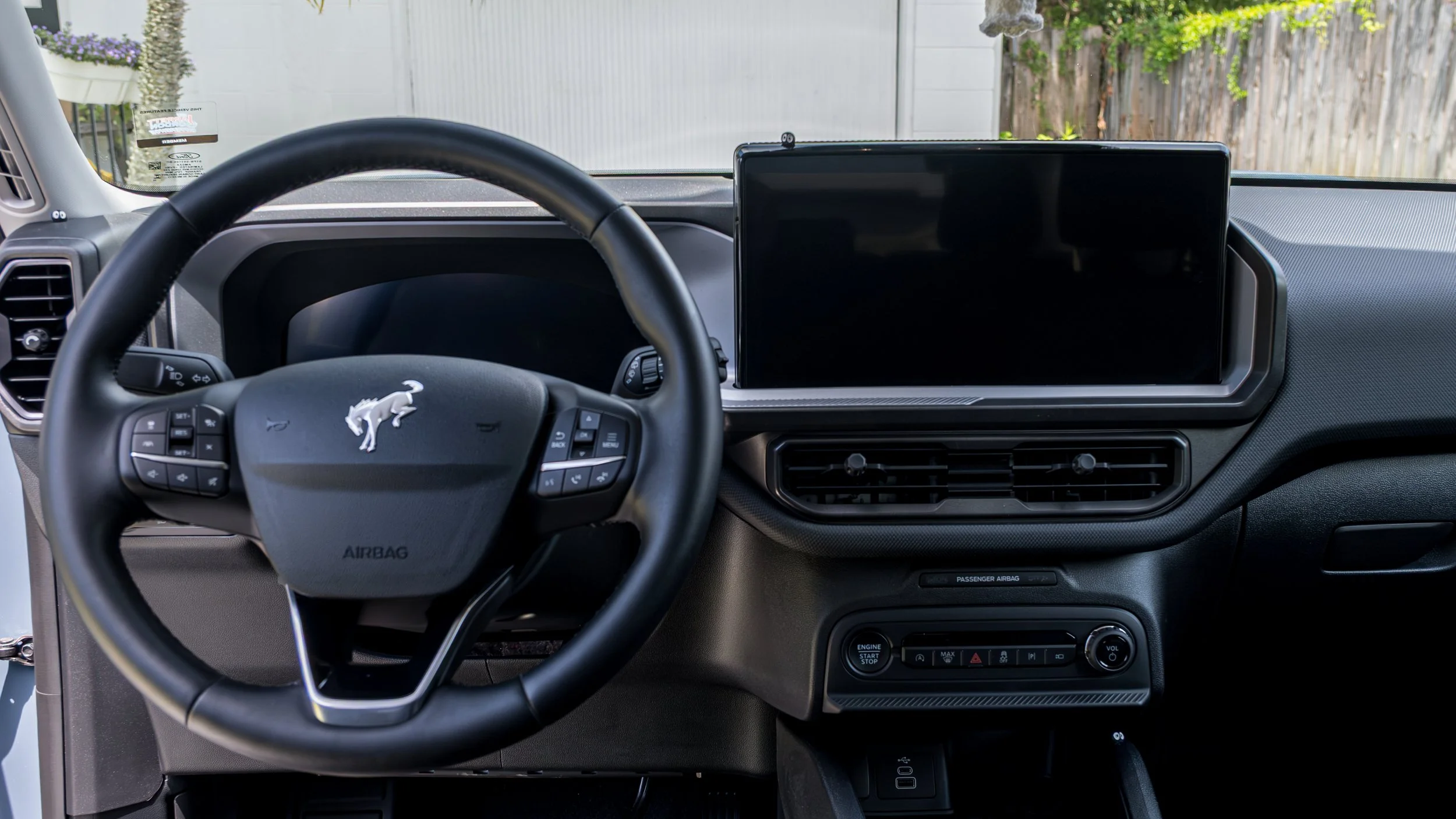Interior view of a vehicle dashboard featuring a steering wheel with a lion emblem, large digital display screen, air vents, and various controls in a modern vehicle.