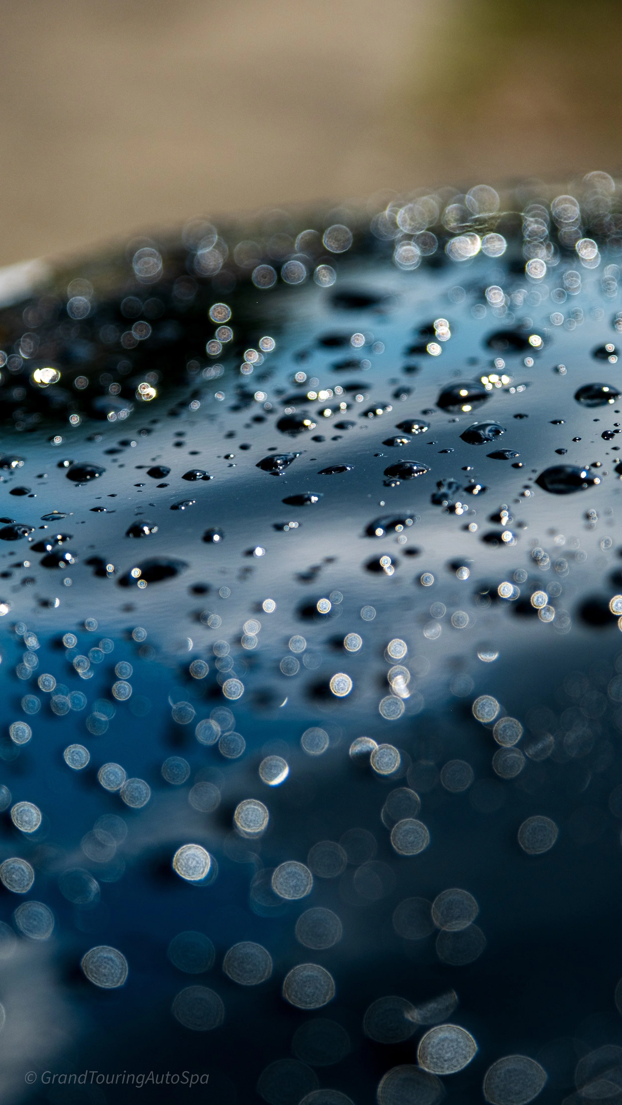 Close-up of water droplets on a dark, shiny surface with a blurred background, creating a bokeh effect.