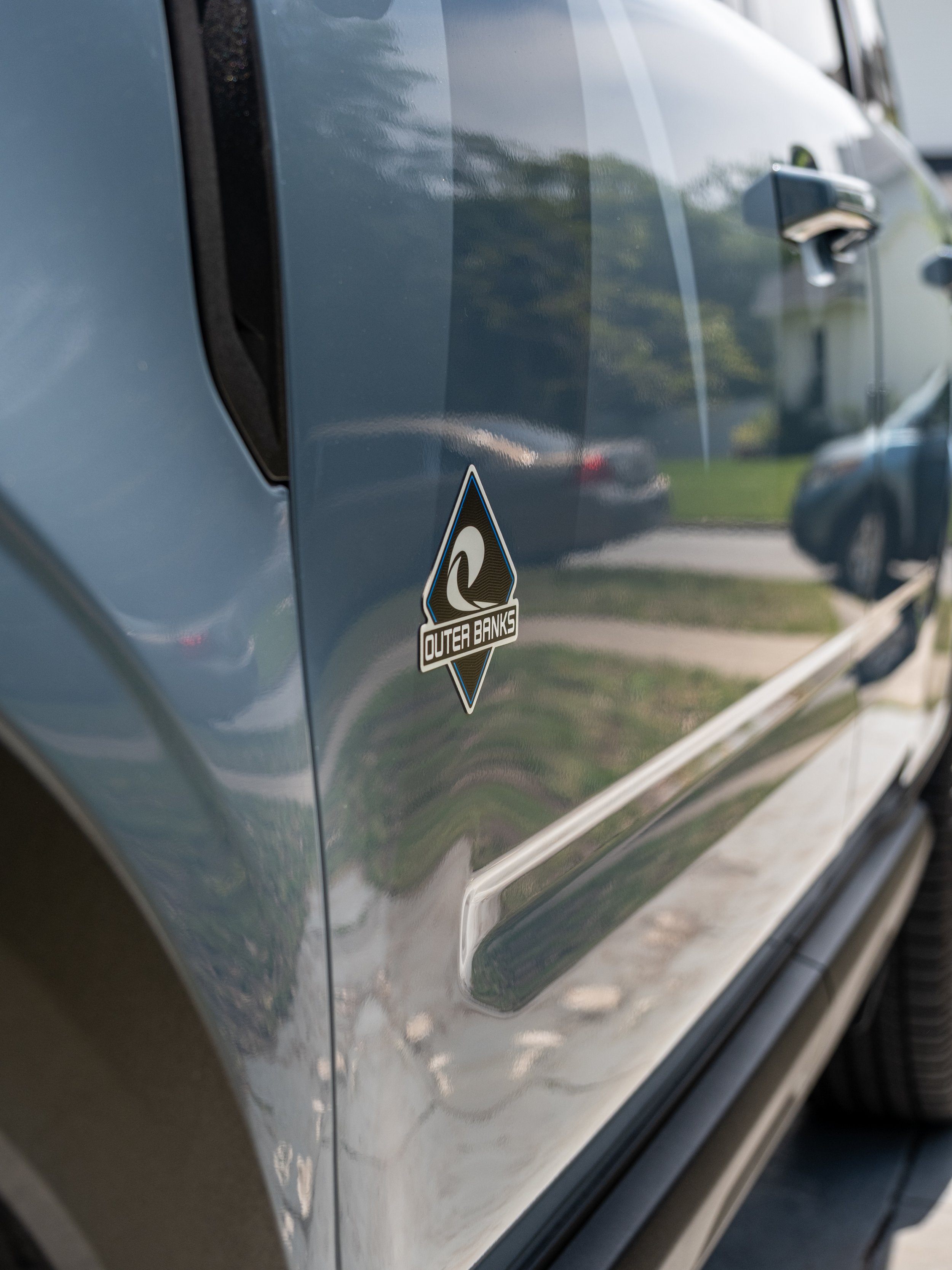 Close-up of a blue vehicle's side with a black and blue logo sticker that says 'Outer Banks'.