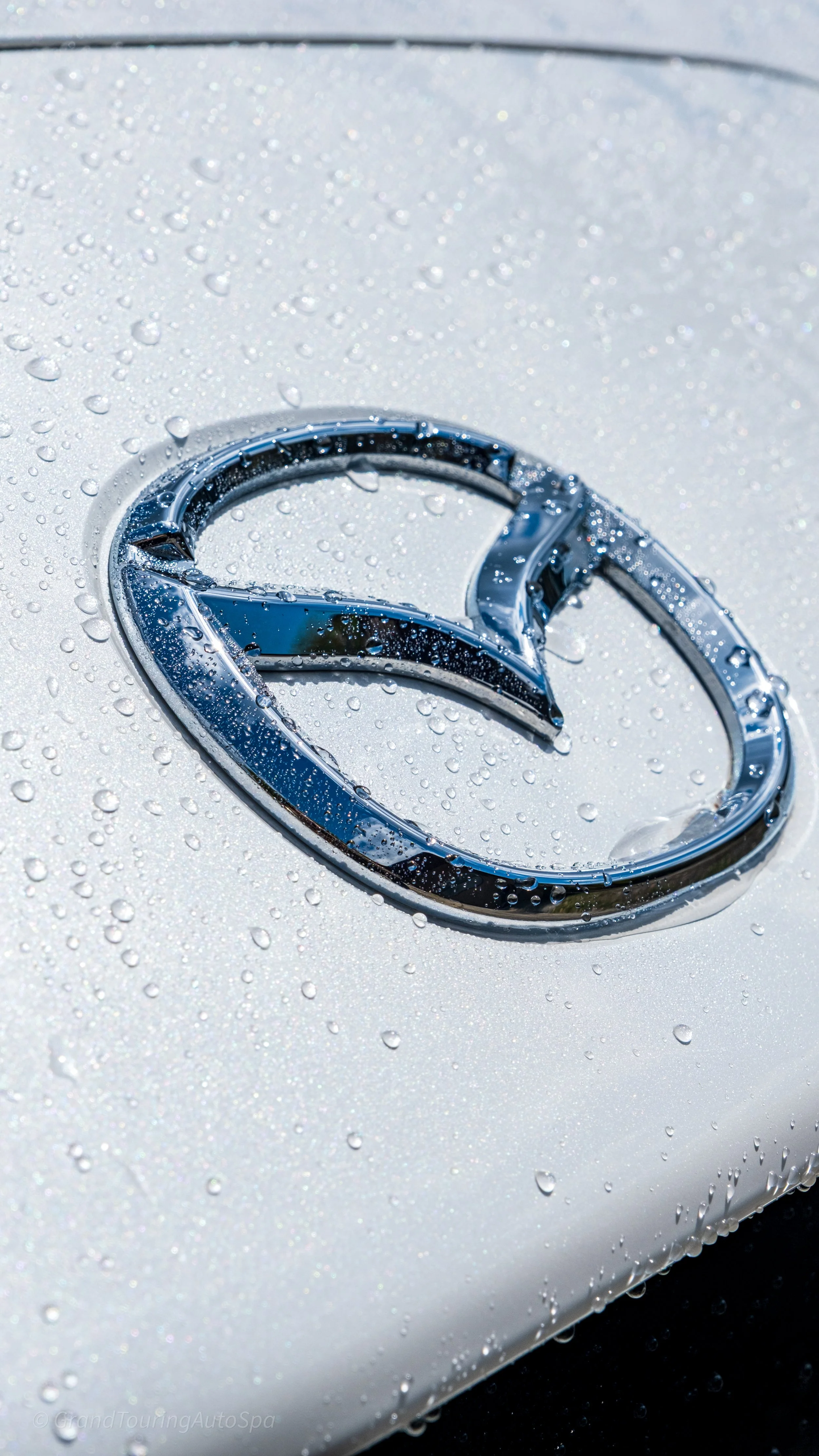 Close-up of a Mercedes-Benz logo on a wet, white car surface with water droplets