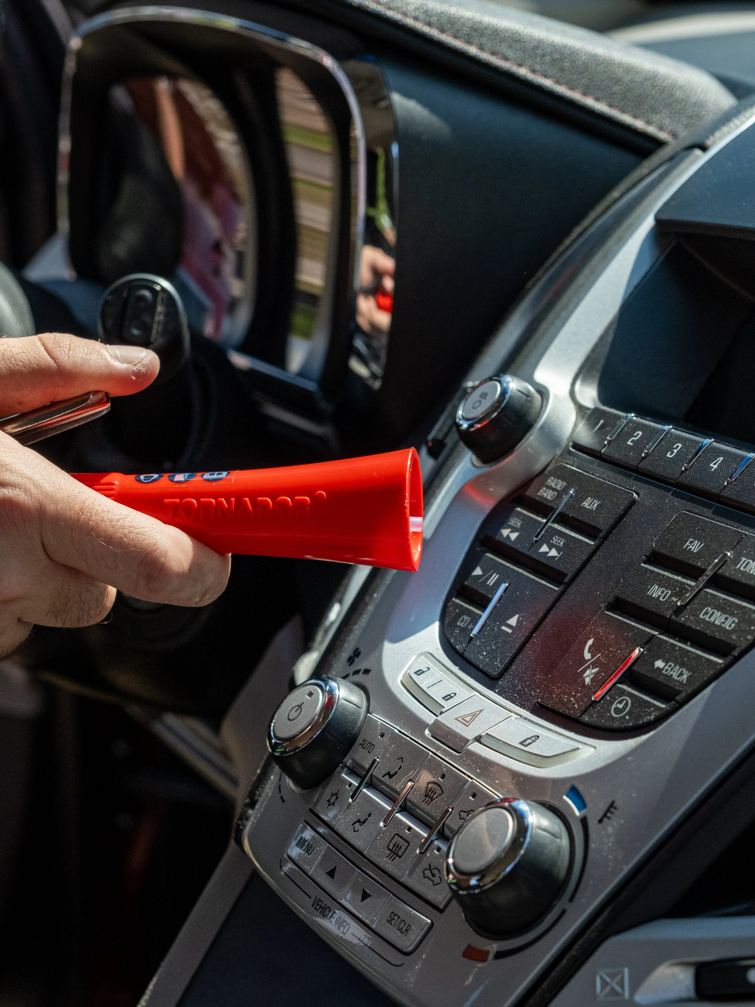 Close-up of a car's dashboard with a person holding a red tornado safety tool near the controls.
