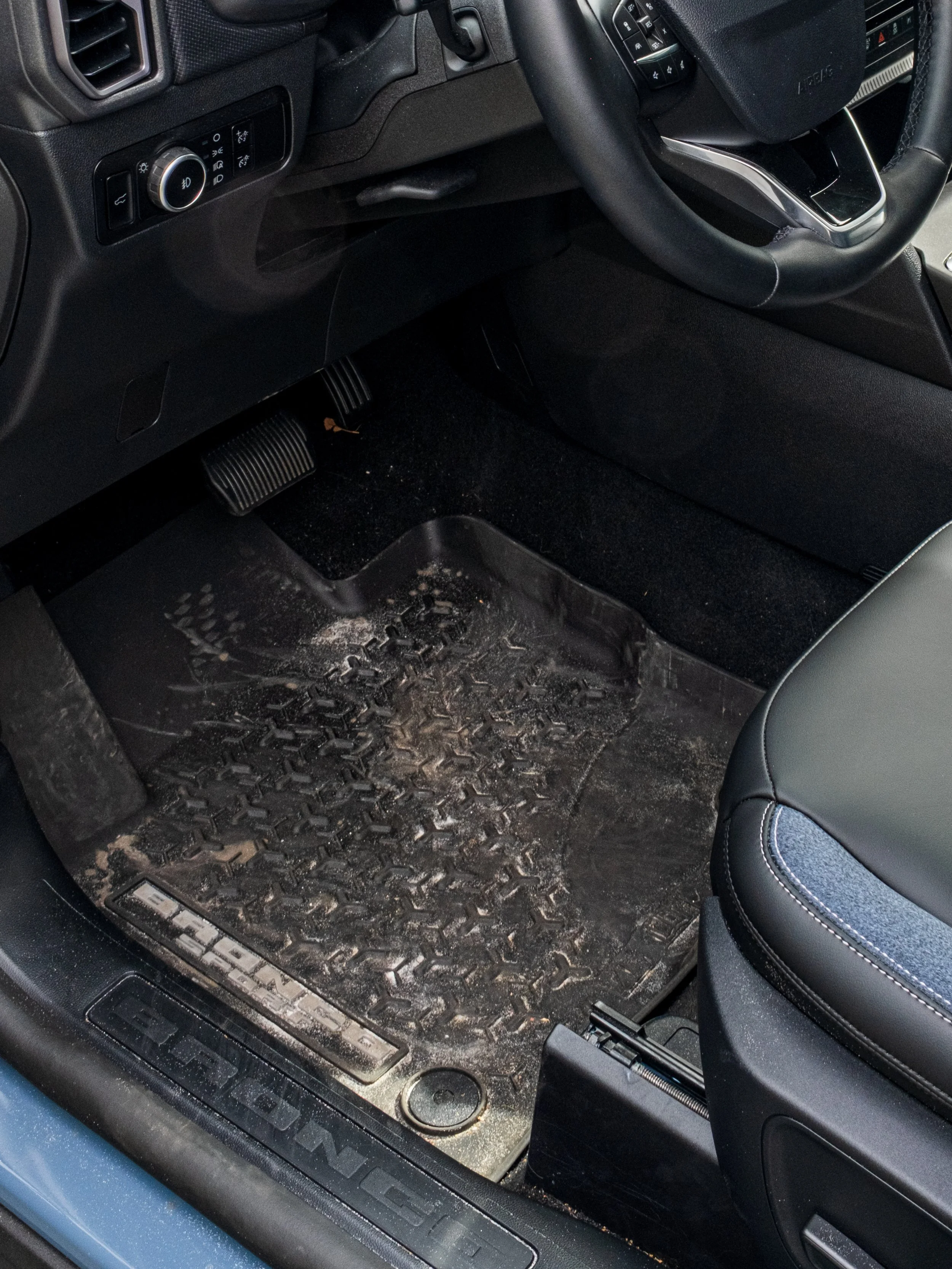 Dirty black rubber car floor mat with dirt and mud, located in the driver's side of a vehicle.