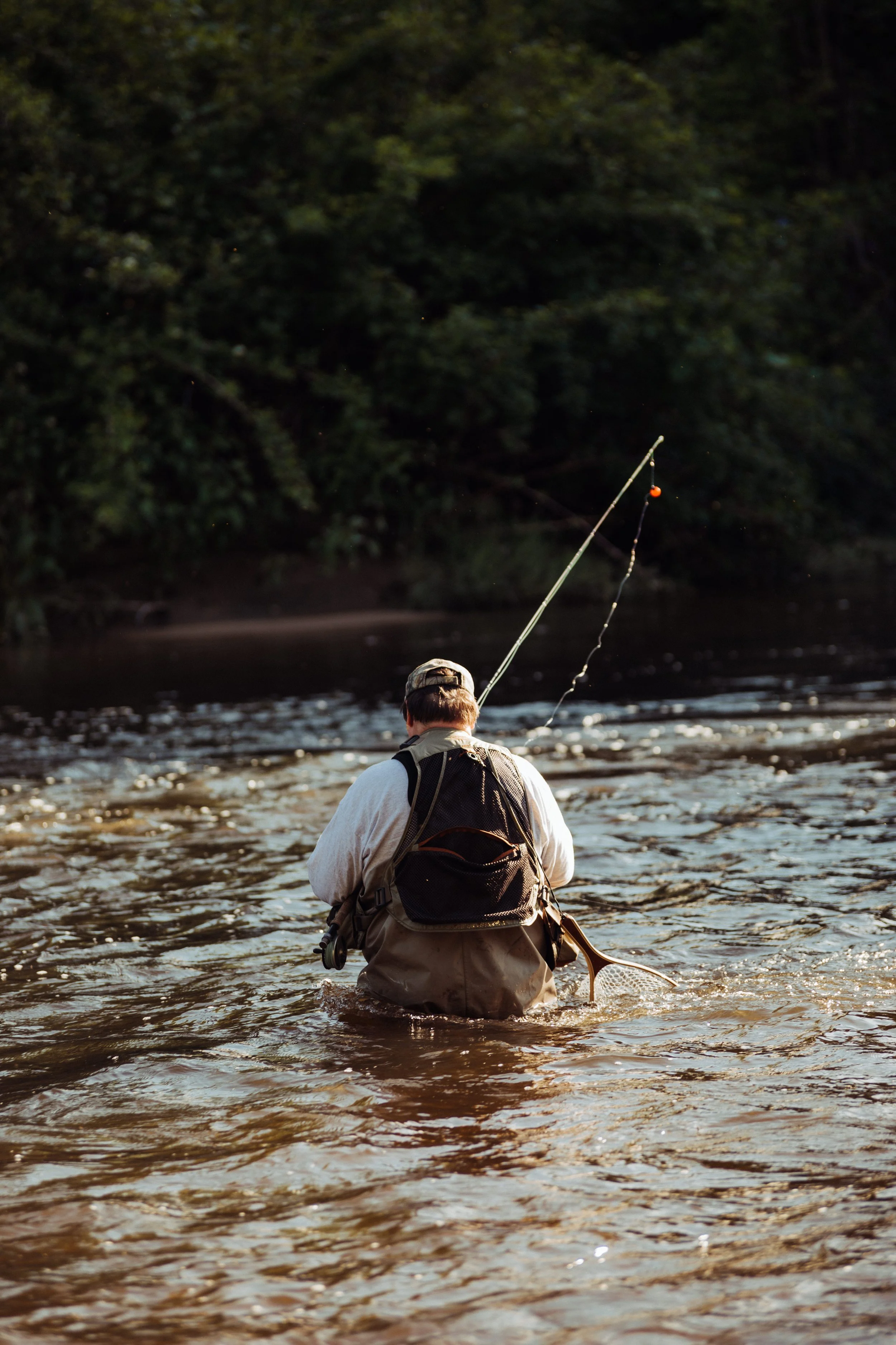 Man fishing in a river with a fishing rod.