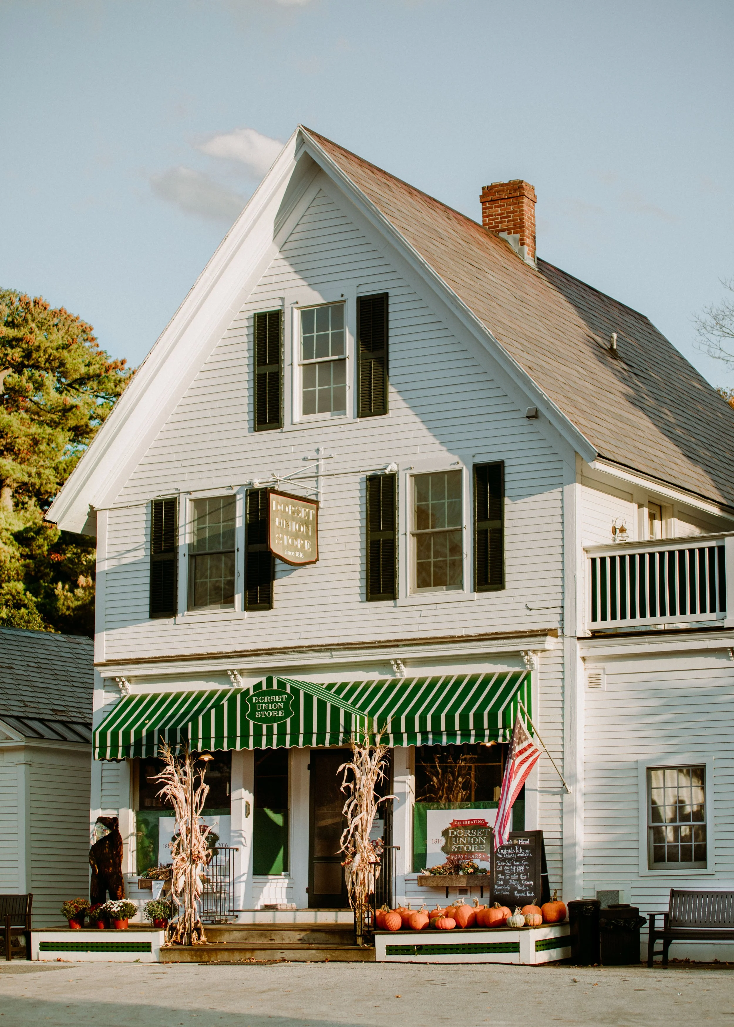 A white, two-story building with a green and white striped awning reads 'Dorset Union Store'; pumpkins and fall decorations are outside, with trees in the background.