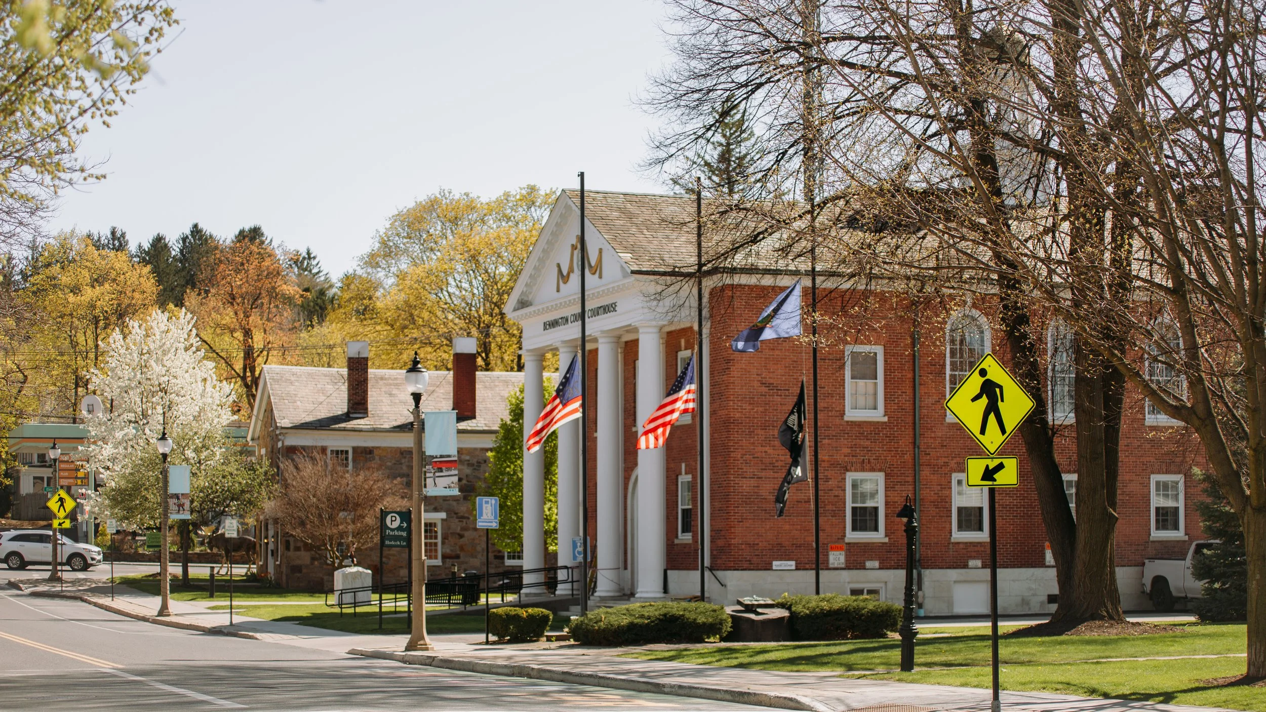 Town square with brick courthouse building, American flags, pedestrian crossing signs, and trees