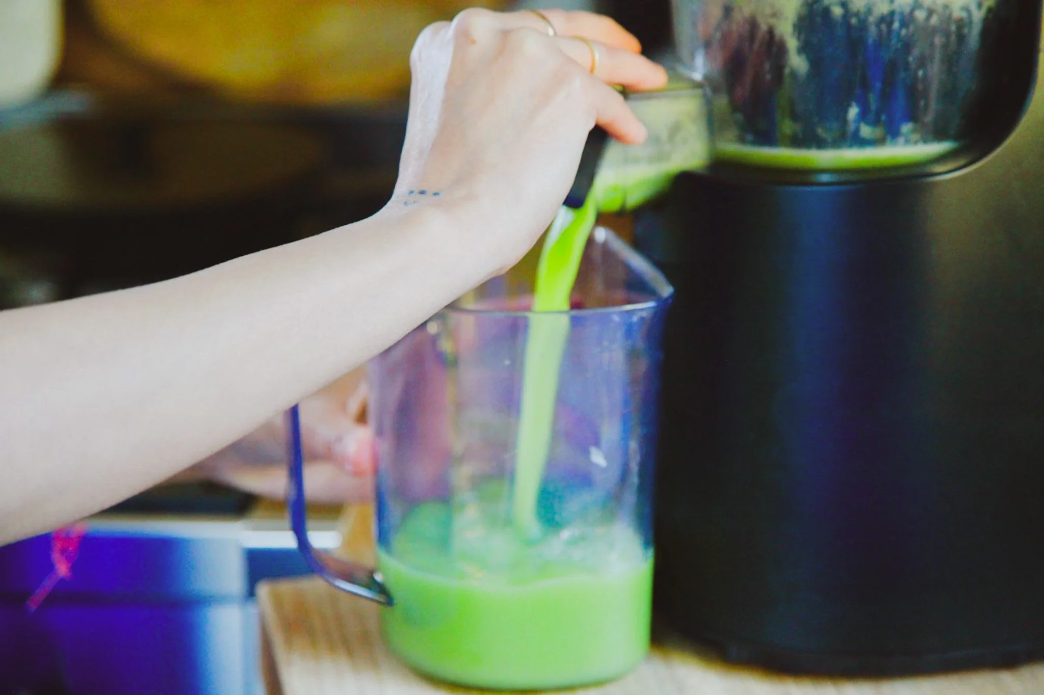 Close-up of a hand pouring green liquid from a container into a clear glass.