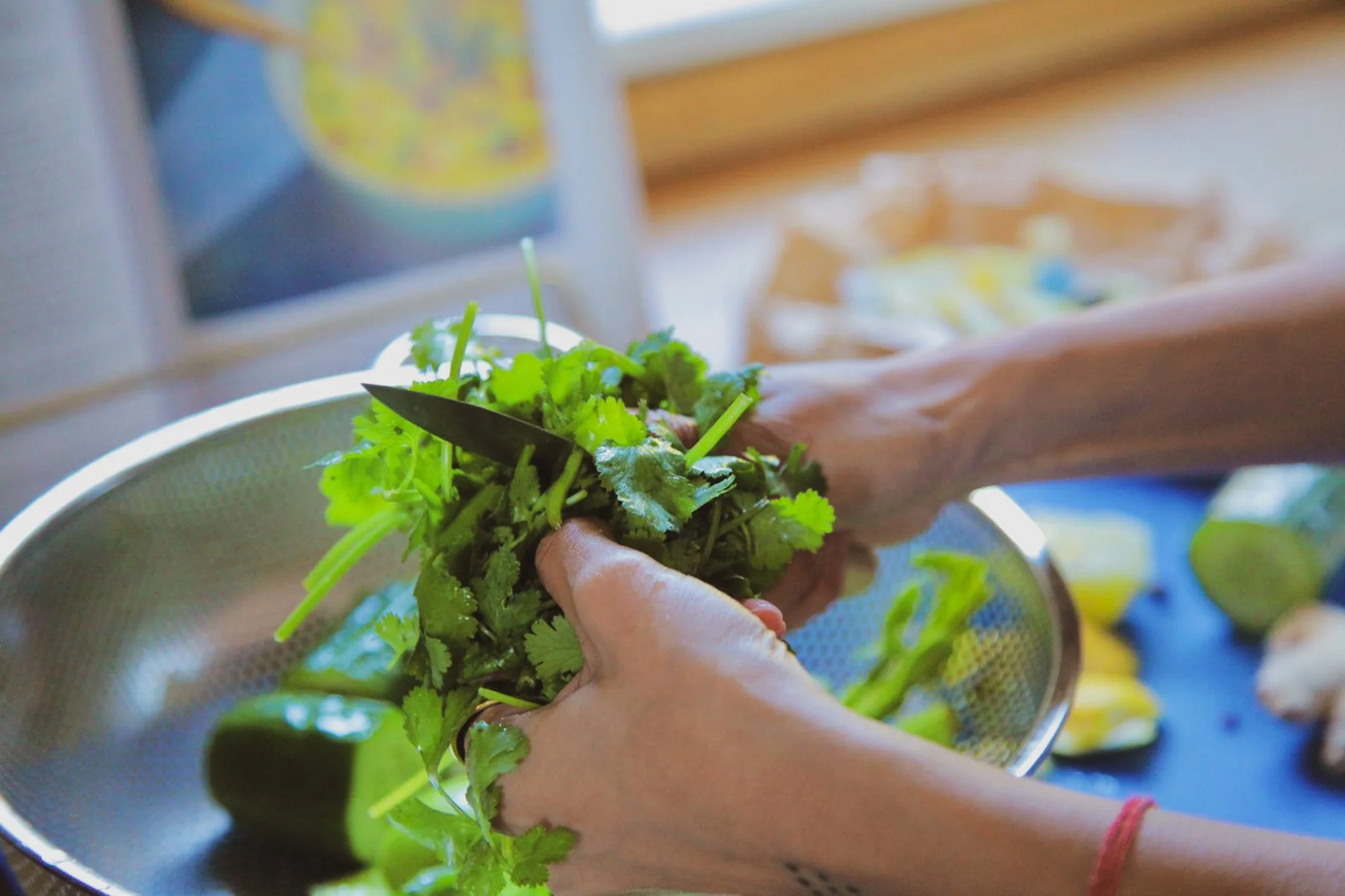 Person washing fresh green herbs in a colander over a sink.