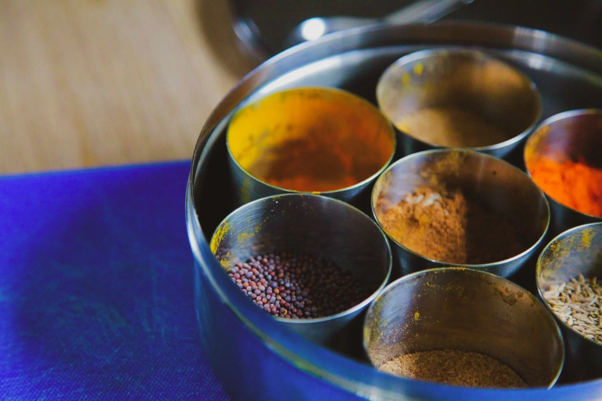 Close-up of metal spice tins containing various spices and herbs, arranged in a circular pattern.