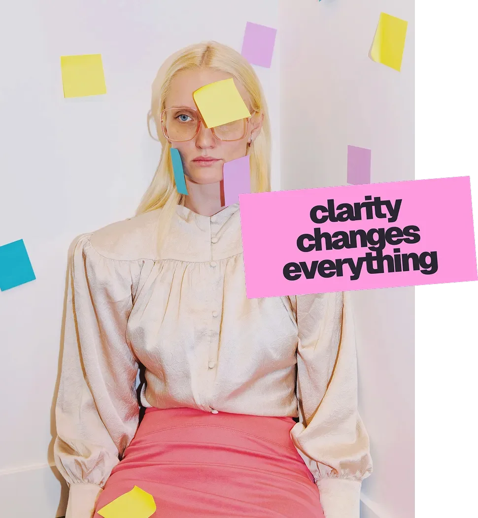A woman with blond hair wearing glasses with yellow, purple, and blue sticky notes on her face and surrounding her. She has a serious expression and is wearing a cream-colored blouse and pink skirt. There is a pink sign with black text that reads "clarity changes everything."
