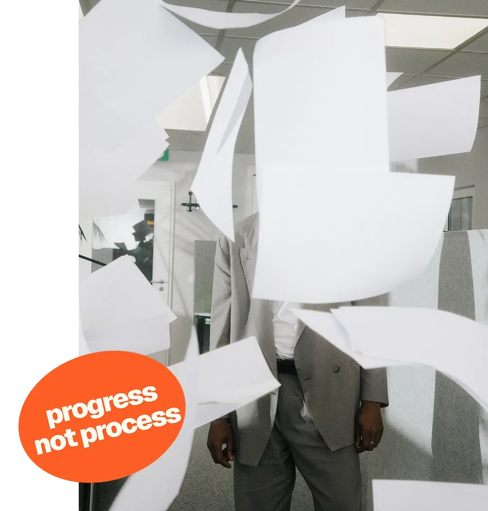 Person in a suit standing behind a shattered glass partition with papers flying around, and a sticker that reads "progress not process" on the glass.