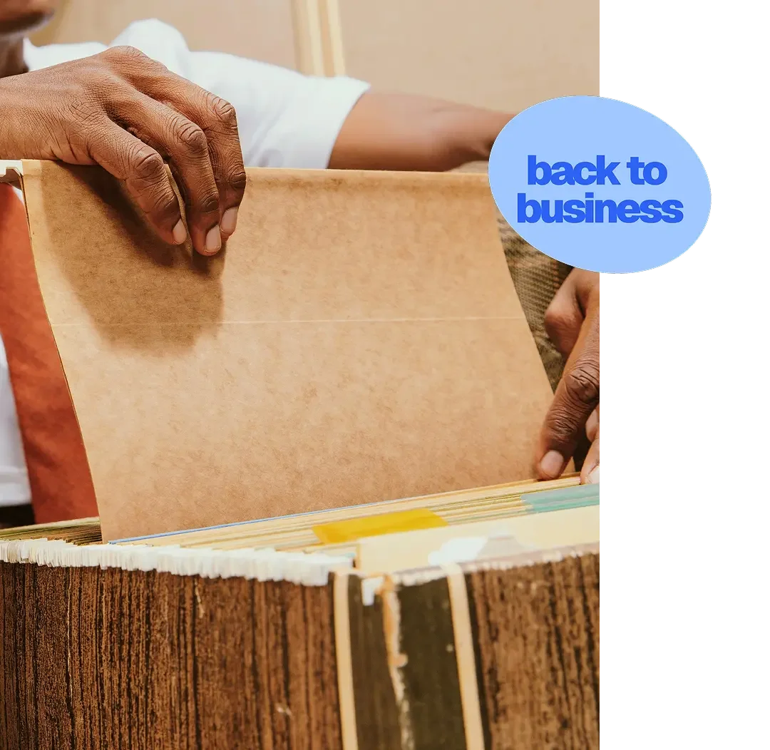A person is flipping through a file folder in a record store or archive, with a blue sticker that says 'back to business'.