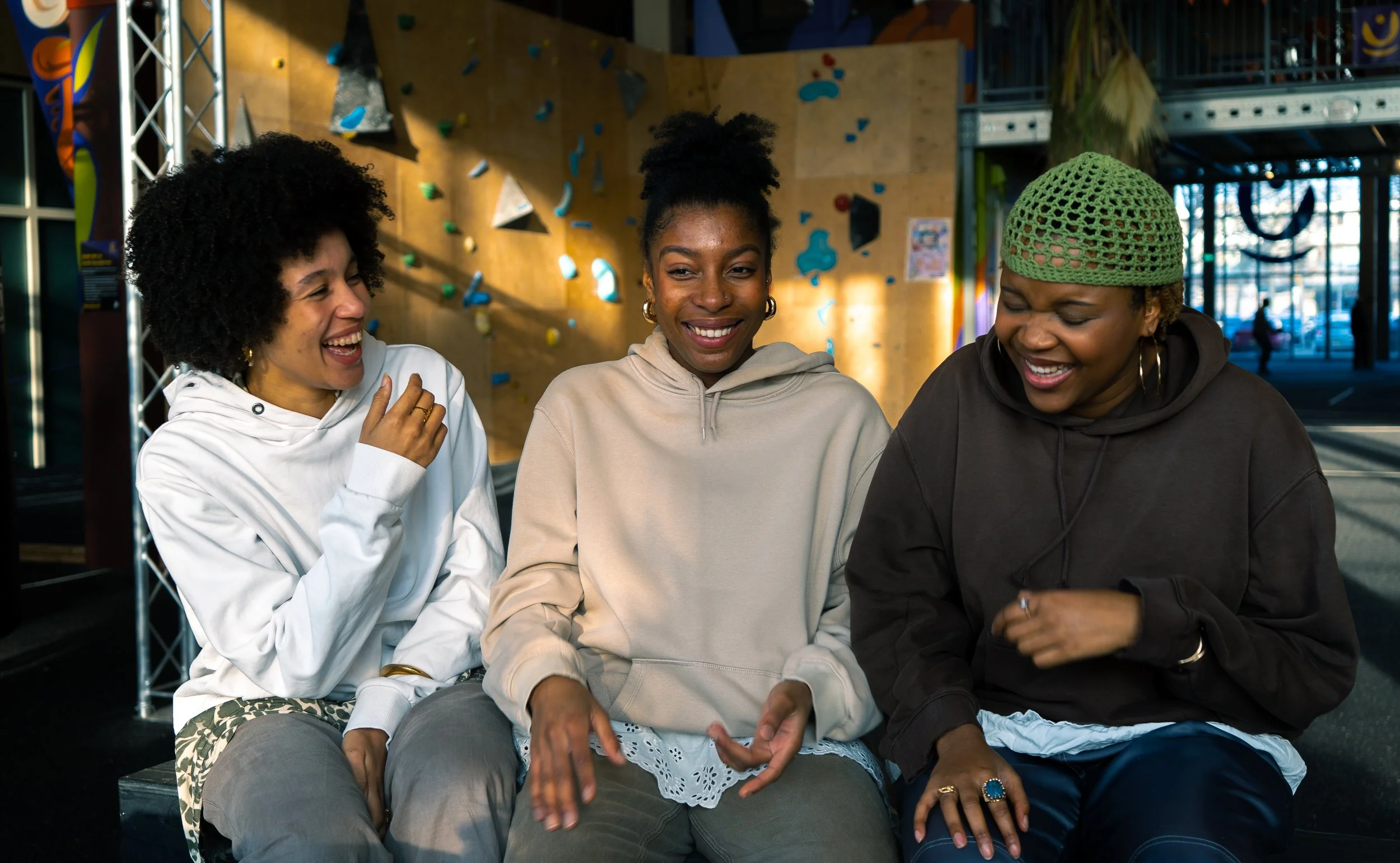 Three women sitting and laughing together inside a climbing gym.