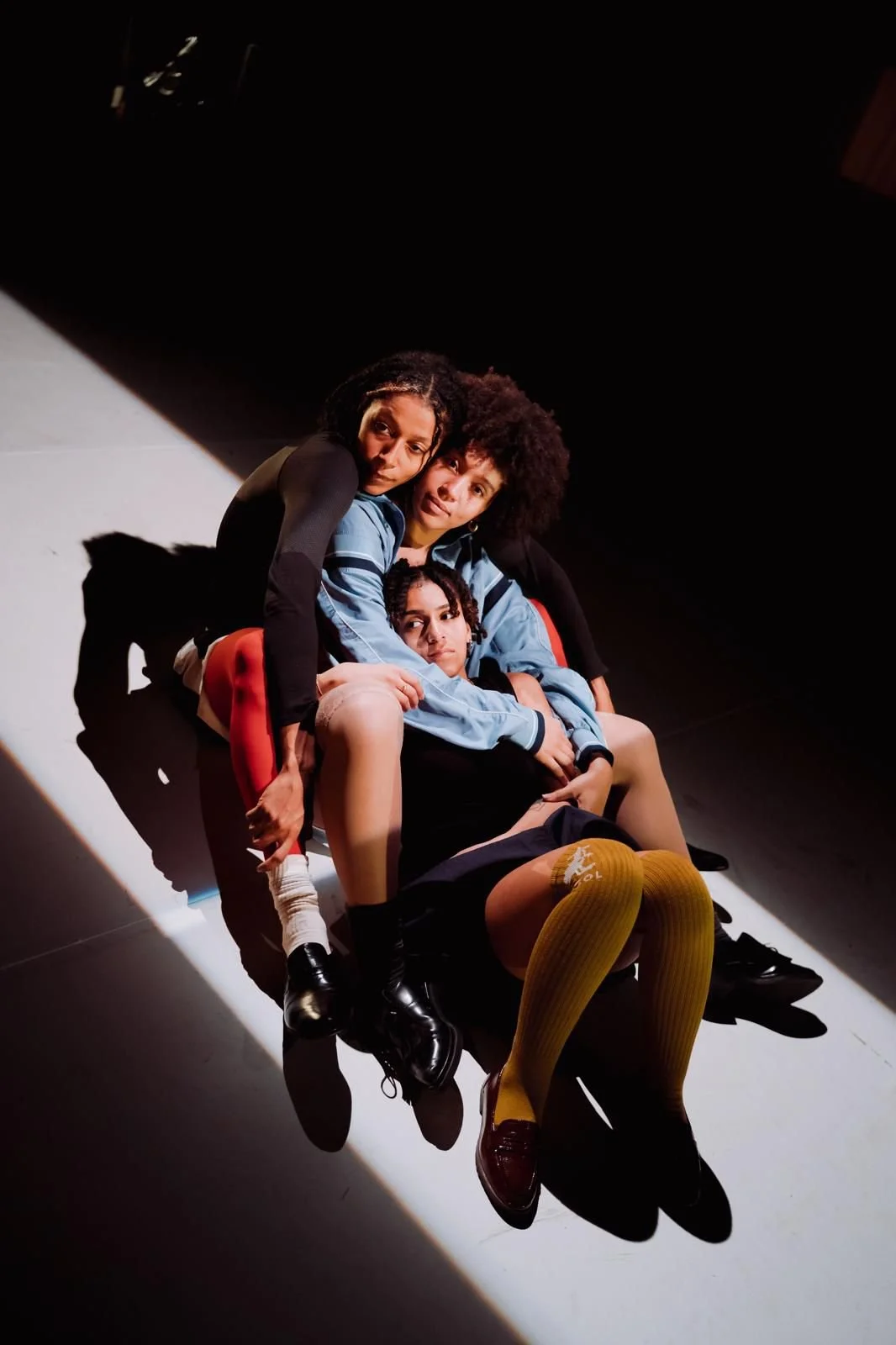 Four young women in school uniforms lying close together on the ground, with dramatic lighting and shadows creating an intense atmosphere.