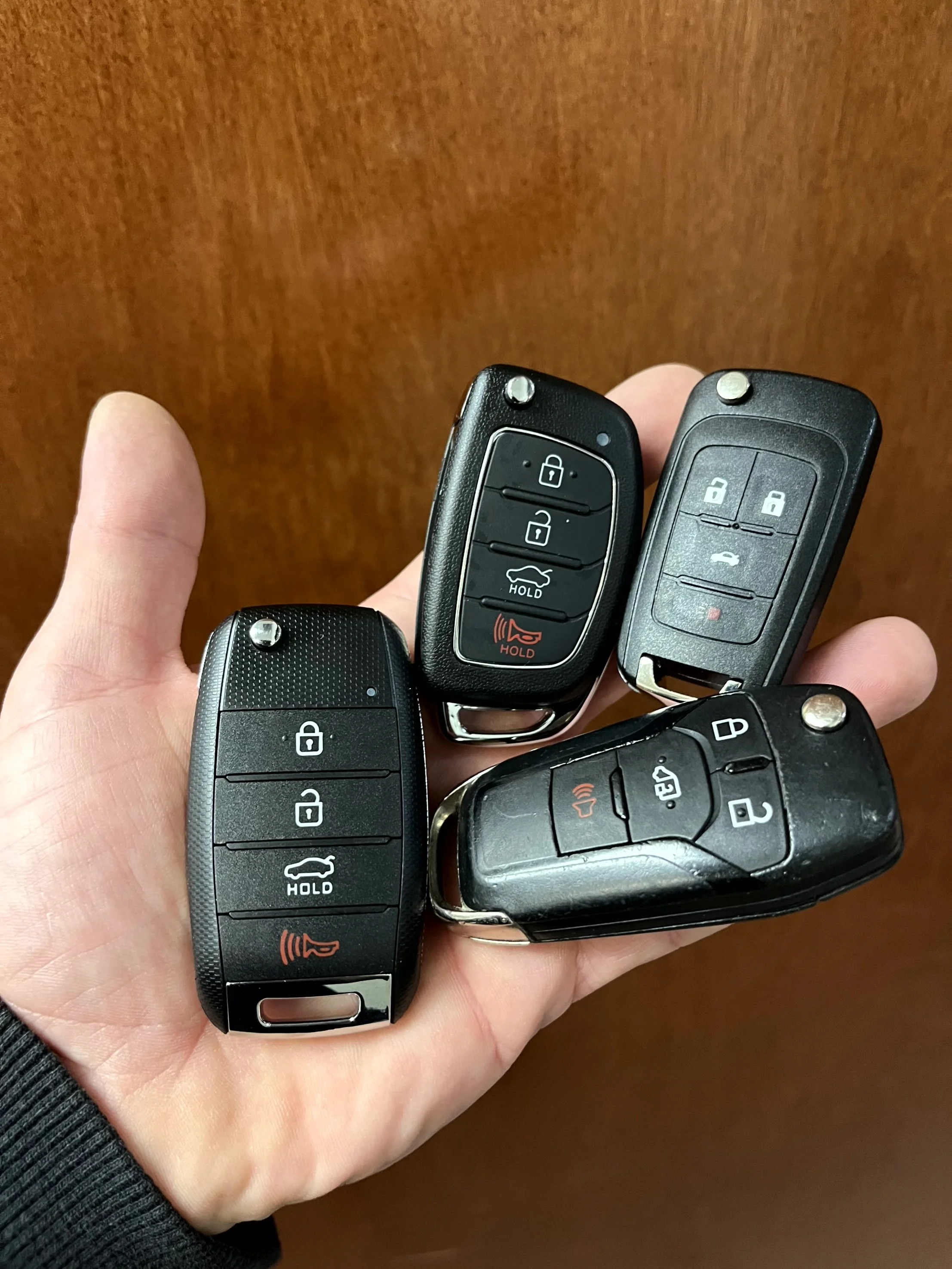 A hand holding four car key fobs against a wooden background.