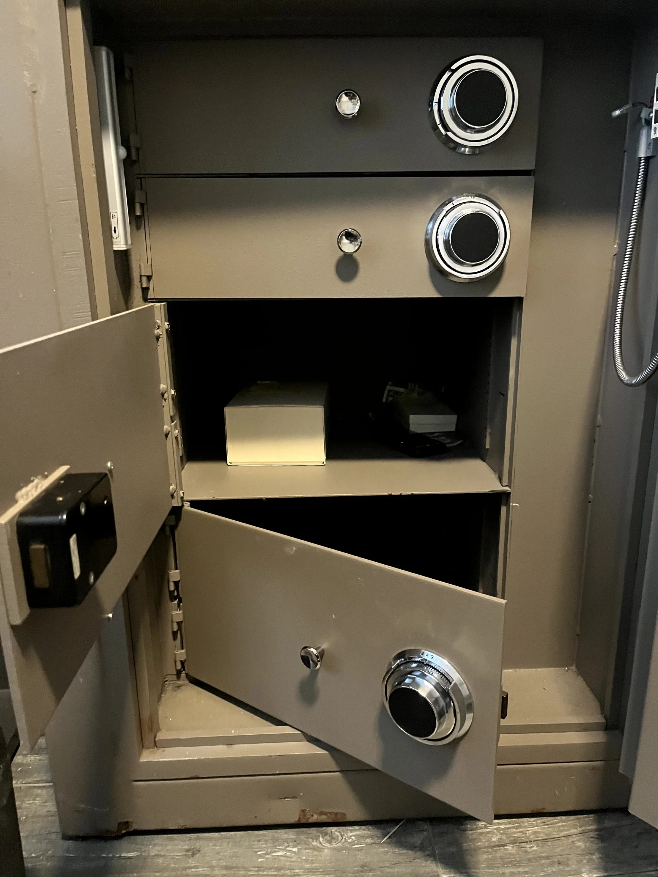 Inside view of a metallic safe showing empty shelves and an unlocked door.