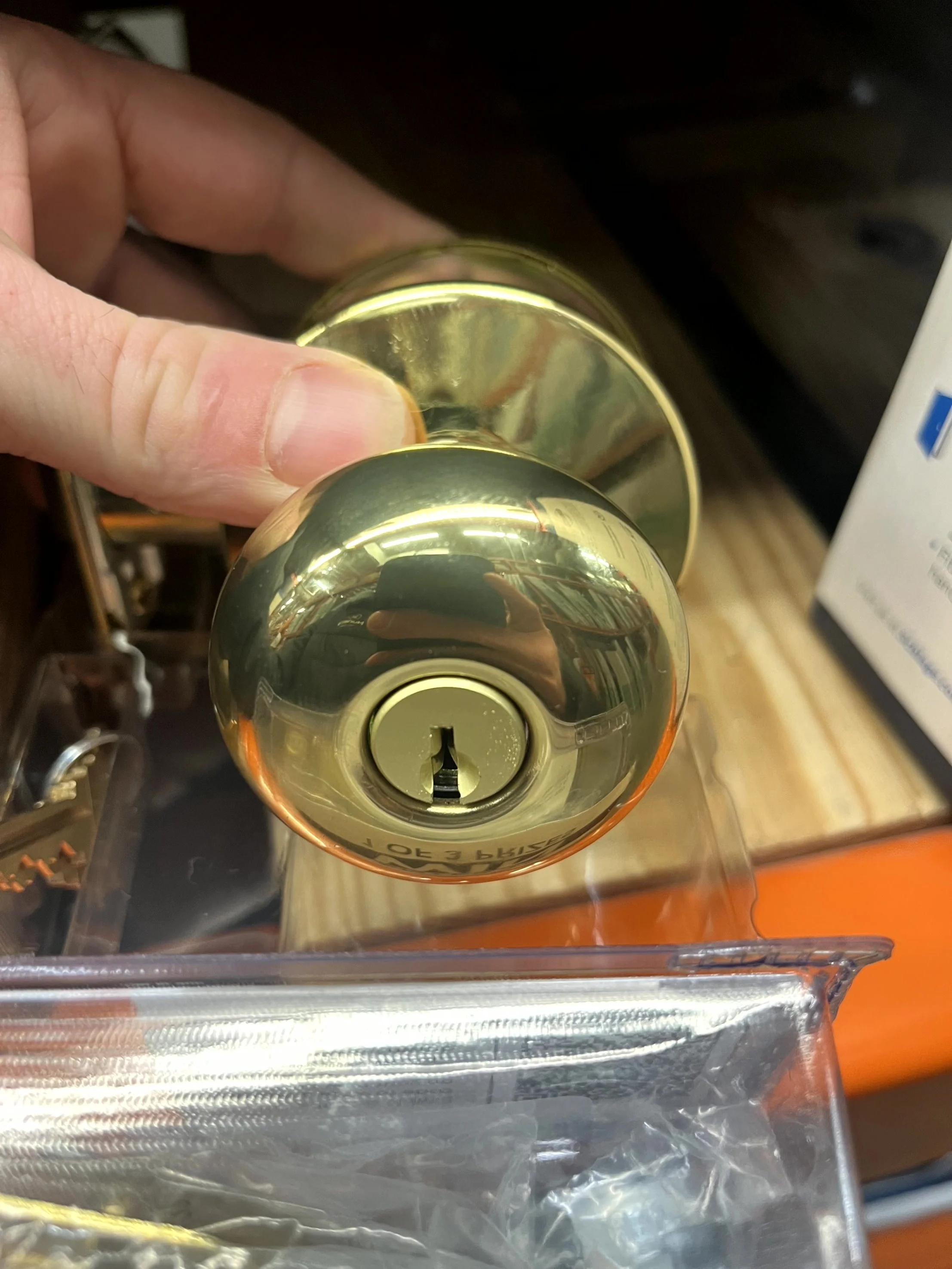 Close-up of a shiny, golden doorknob with a keyhole, being held by a person's hand, with a plastic storage container in the foreground.