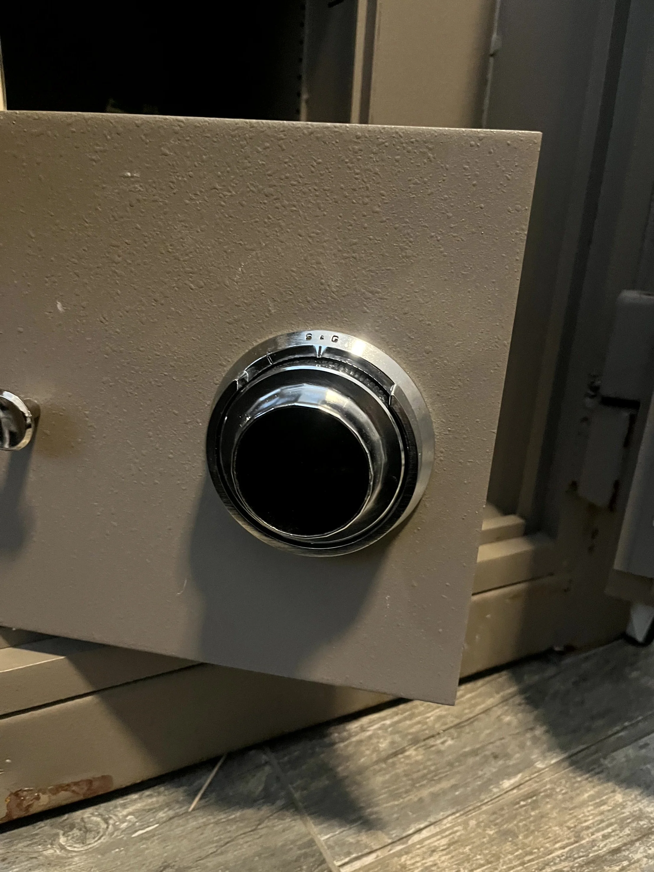 Close-up of a beige metal box with a black circular dial on the front, mounted on a wooden surface, with a dark background.