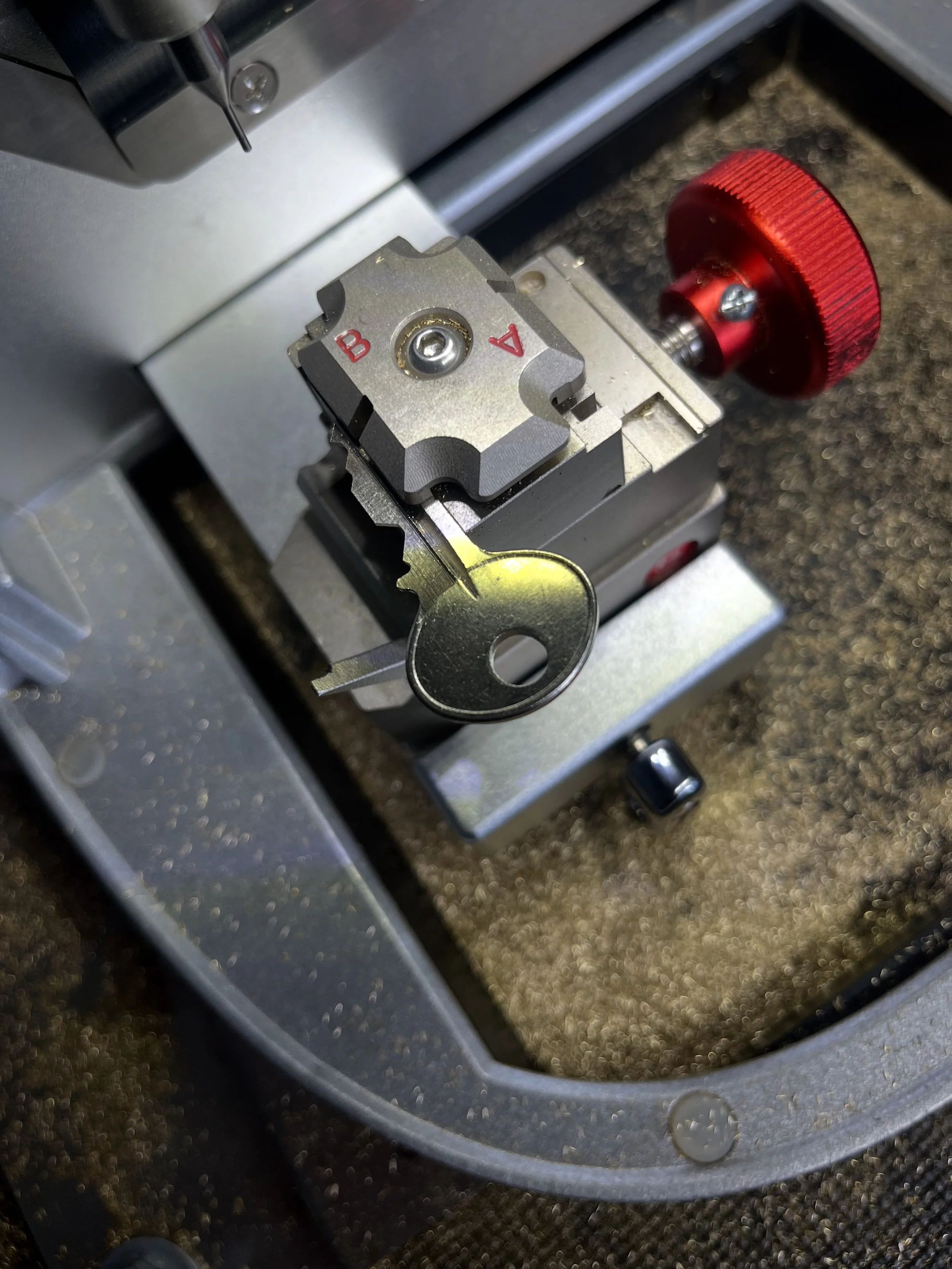 Close-up of a specialized metal machine with a red knob and a metal key, used for precision tasks, on a textured surface.