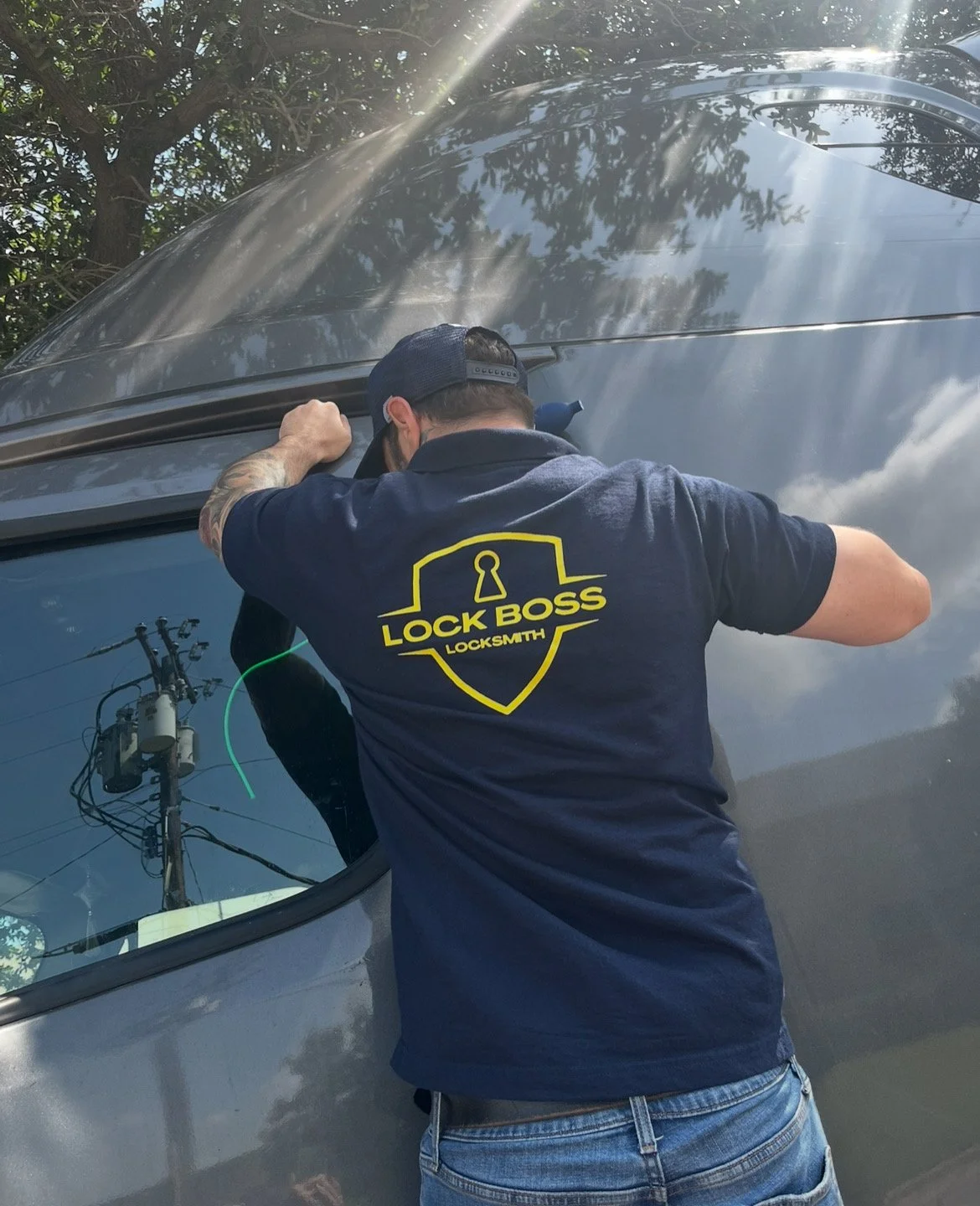 A locksmith wearing a navy t-shirt with a logo that reads 'Lock Boss Locksmith' working on a car door.