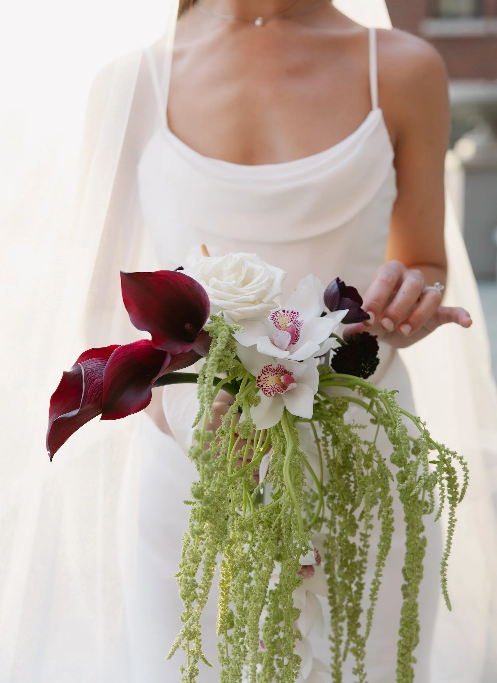 Top Spokane Florist creates a stunning cascading bouquet of white roses, orchids, dark calla lilies, and green hanging amaranthus.