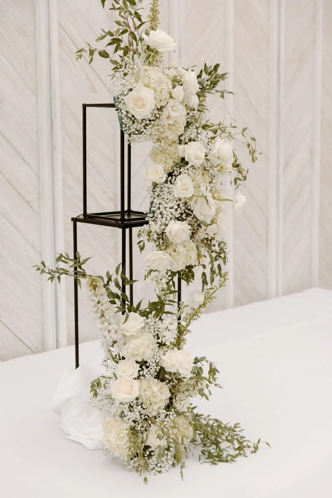 White floral arrangement with roses and baby's breath on a black metal stand available for rent