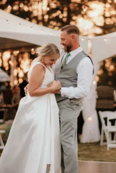 A bride and groom dance outdoors at sunset in Spokane, with the bride wearing a white wedding dress and the groom in a gray vest and white shirt.