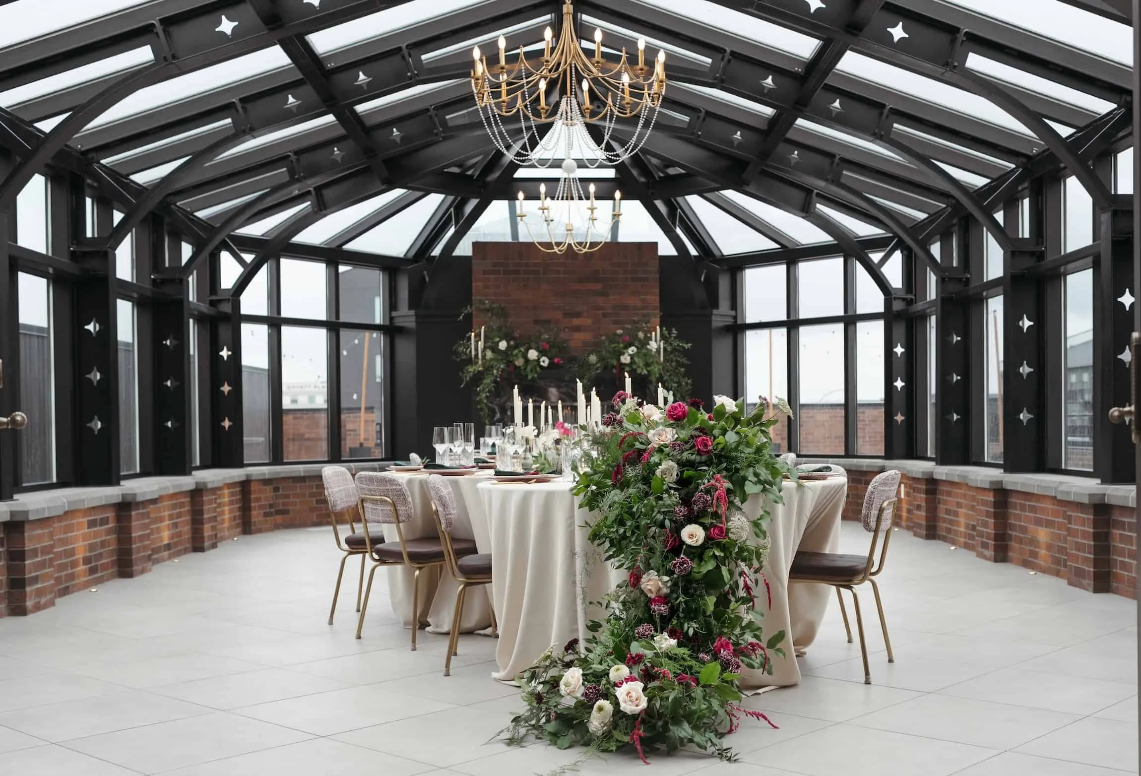 Wedding in a glass-enclosed rooftop venue at Kindred & Co in Post Falls, Idaho, decorated with a large floral arrangement and several candlesticks, with a brick fireplace at the back and chandeliers hanging from the ceiling.