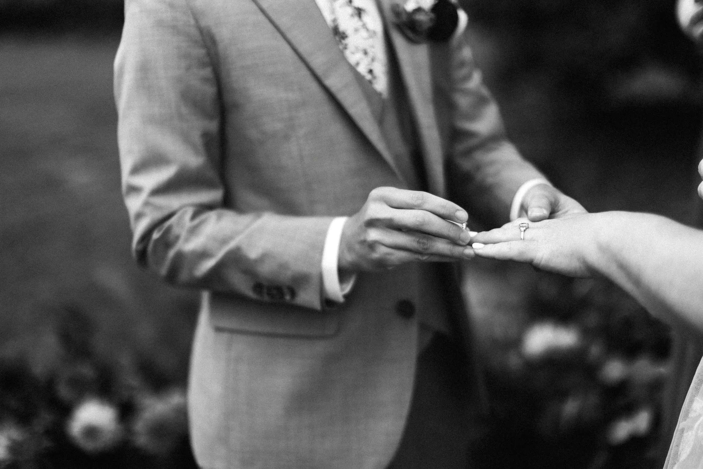 A wedding ceremony in Spokane where a person in a suit is placing a ring on a woman's finger.