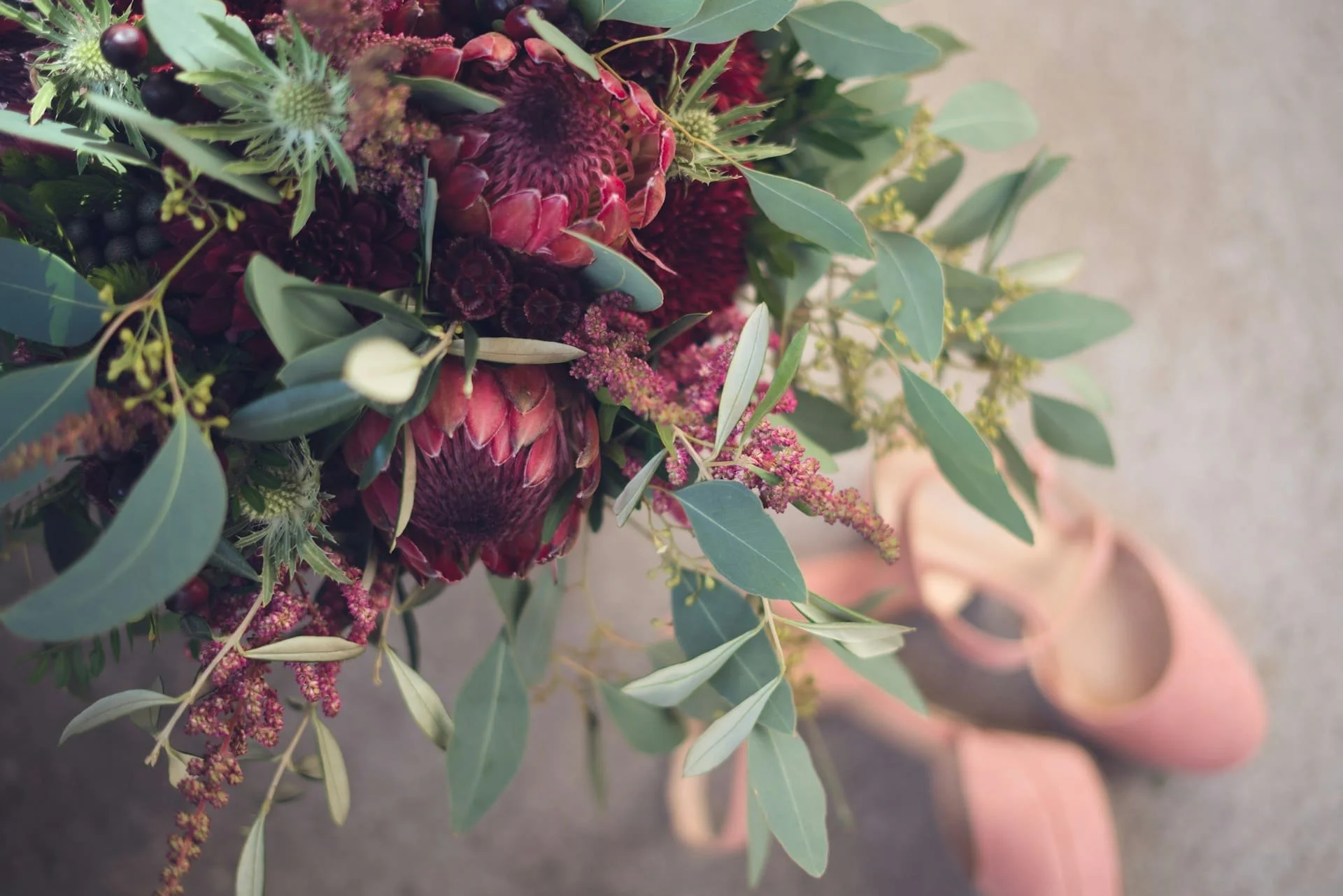 A bouquet of dark red flowers and green leaves, placed on the ground in front of pink shoes in Spokane