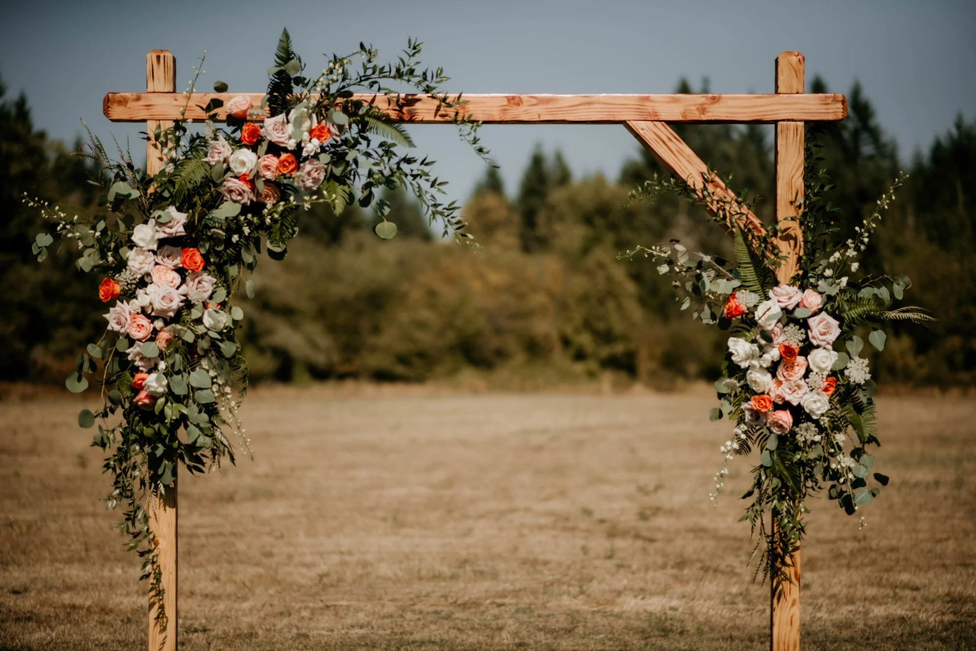 Spokane's Top Wedding Florist showing off a wooden arch decorated with pink, white, and orange flowers, as well as green foliage, at a wedding venue in Idaho.