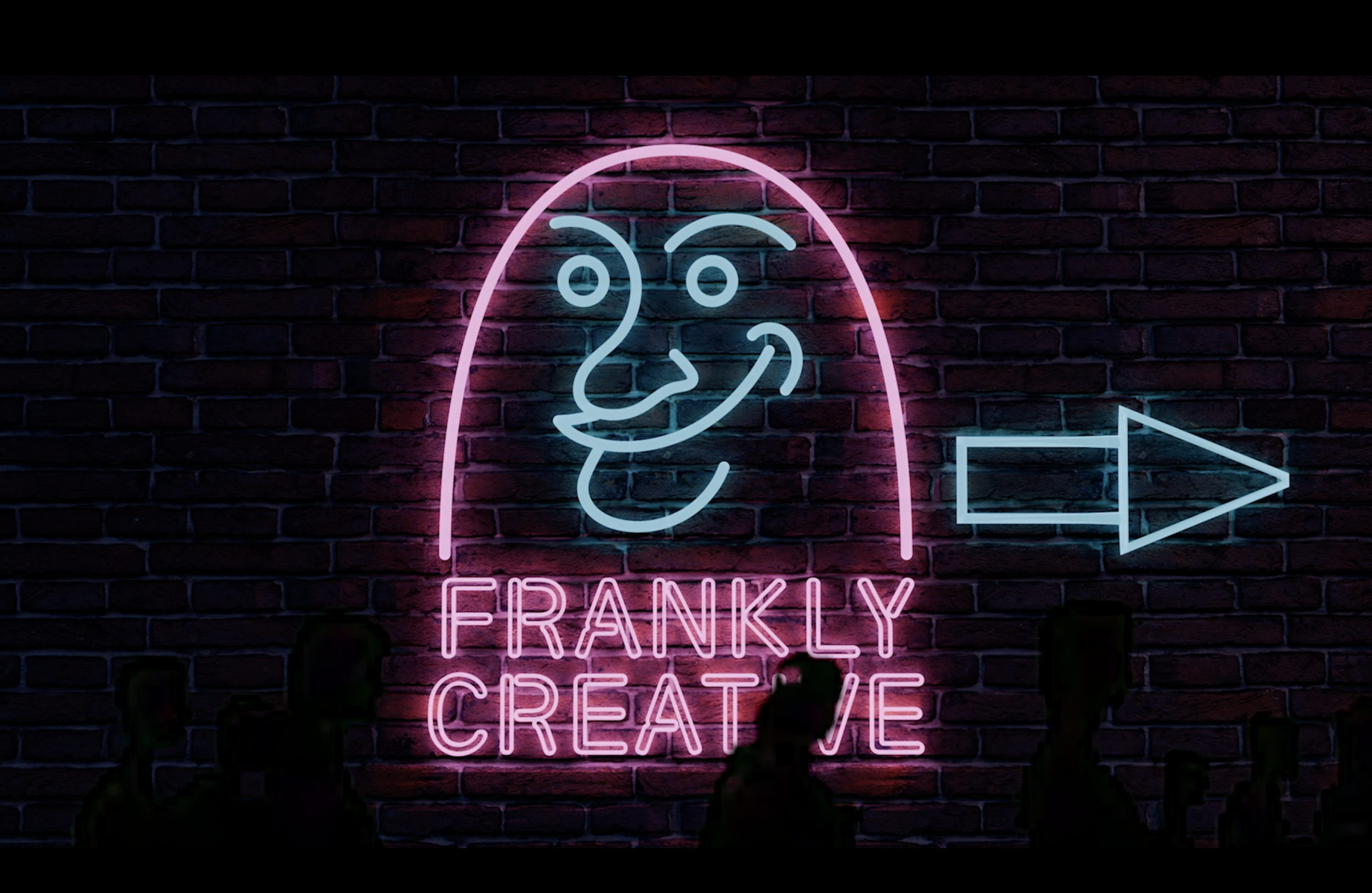 Neon sign on a brick wall with a drawing of a face sticking out its tongue, the phrase 'FRANKLY CREATIVE' below, and an arrow pointing to the right.