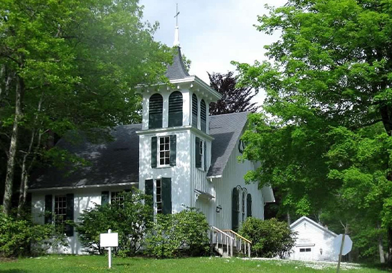 White church with steeple surrounded by green trees in a lush yard.
