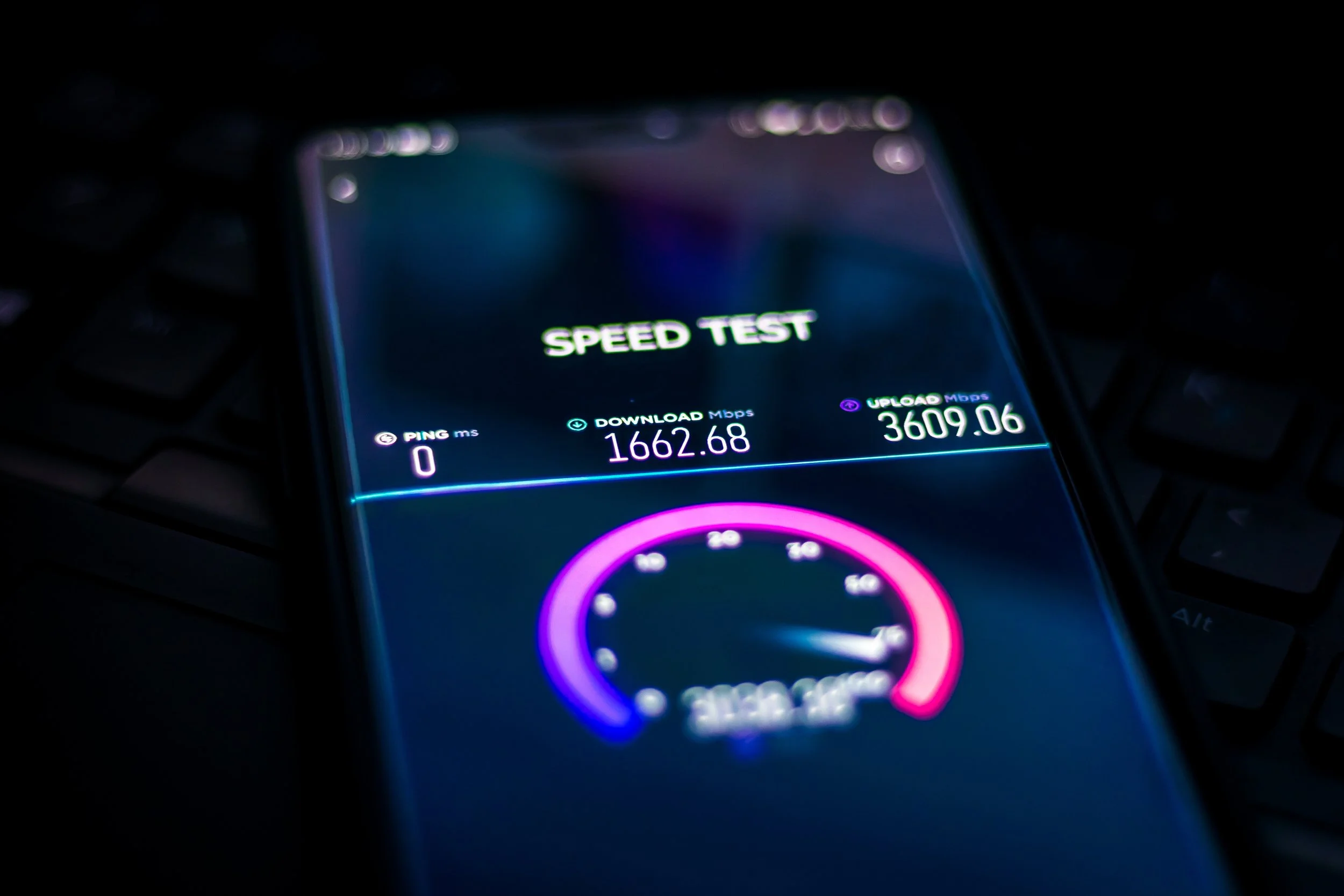 A smartphone screen displaying a speed test with download speed of 1662.68 Mbps, upload speed of 3609.06 Mbps, and ping of 0 ms, illuminated in a dark environment.