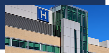Exterior of a hospital building with a blue 'H' sign and modern glass and brick architecture.