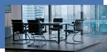Empty modern conference room with six chairs around a rectangular table, large glass windows showing cityscape outside.
