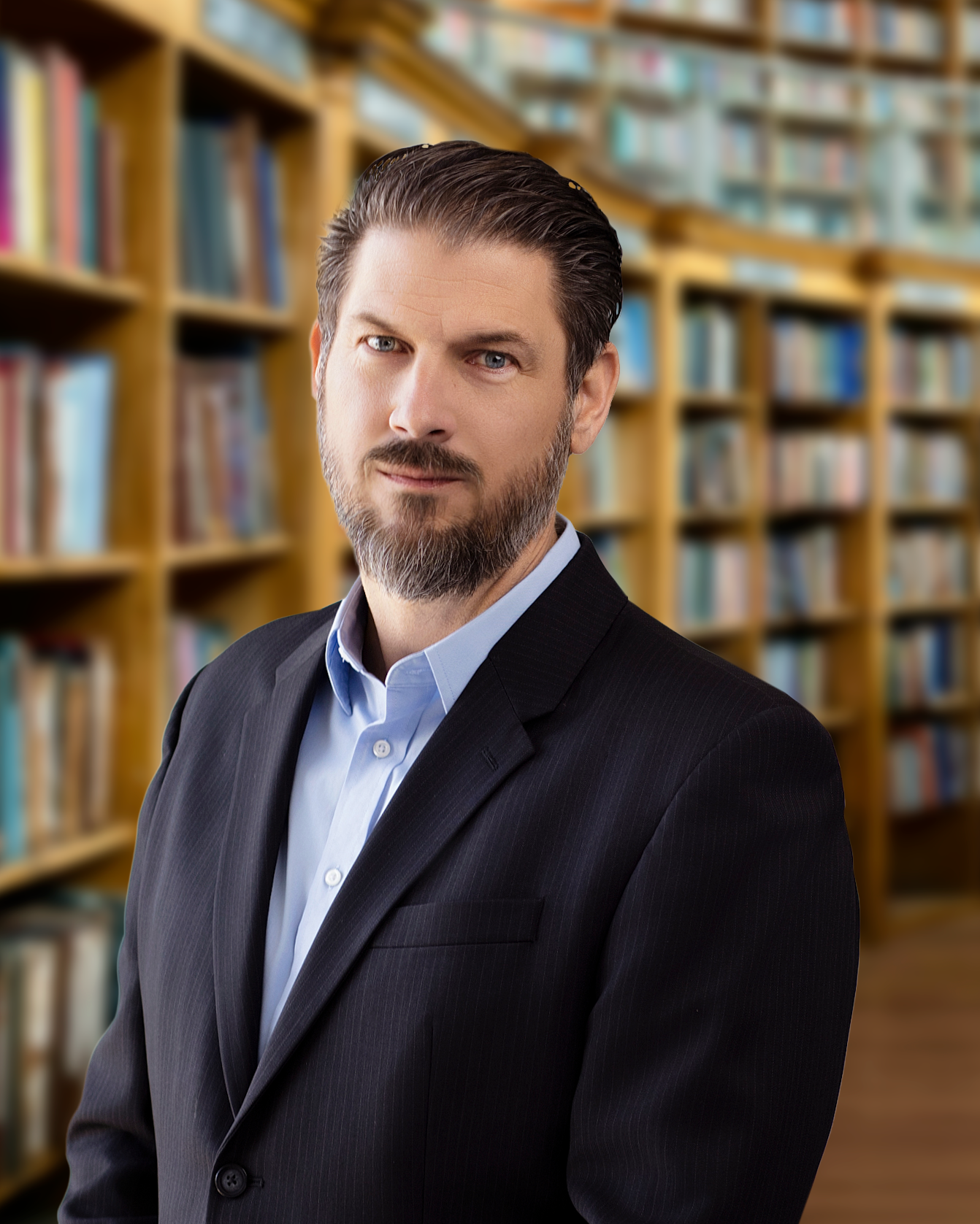 A man in a black suit with a blue shirt standing in a library with shelves of books in the background.