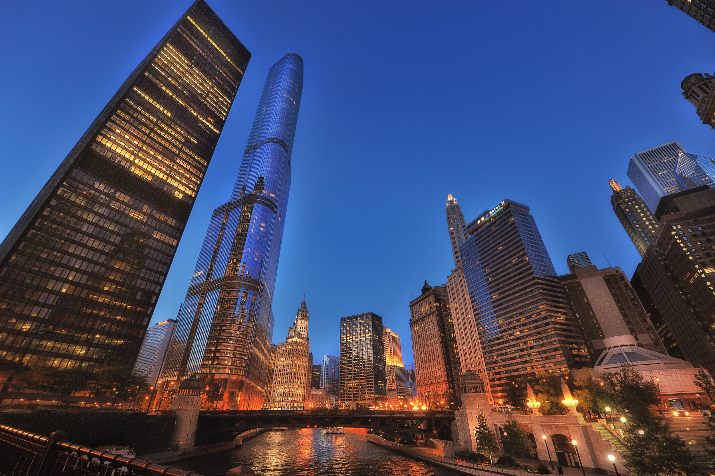 View of skyscrapers in downtown Chicago during sunset, reflecting on the waters of the river with city lights starting to turn on.