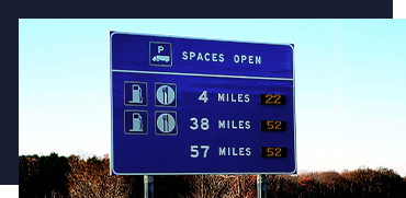 Blue highway sign indicating open parking spaces and distances to nearby towns or locations.