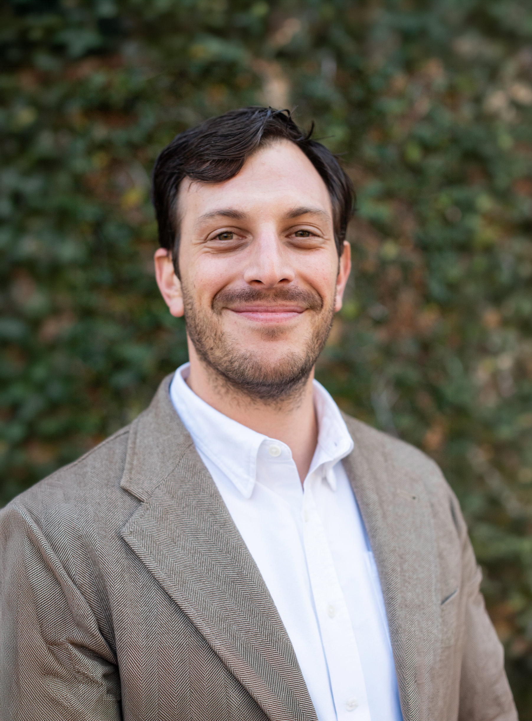 Smiling man in a beige blazer and white shirt outdoors