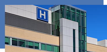 Hospital building with an H sign, glass windows, and modern architecture against a blue sky.