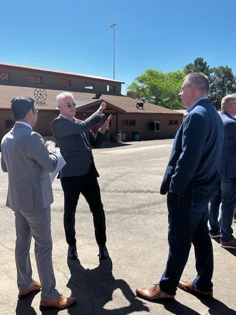A group of men in suits standing outdoors, with one man gesturing while speaking to the others.
