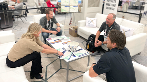 Four people sitting around a coffee table in a lounge area at a conference or event, engaged in conversation.