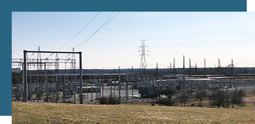 Power lines and electrical substation in a grassy area under a clear sky.
