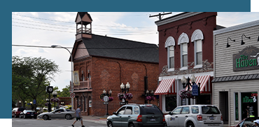 Street view of small town with brick buildings, a clock tower, and parked cars.