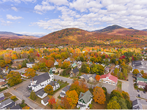 Aerial view of a town with colorful fall foliage, houses, and surrounding mountains