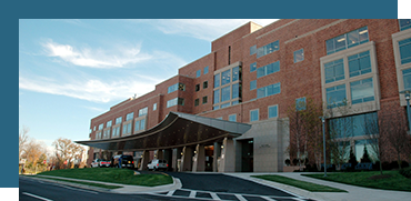 Exterior of a modern brick hospital building with a curved entrance and parking lot.