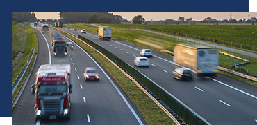 Several cars and trucks driving on a multi-lane highway with green fields in the background.